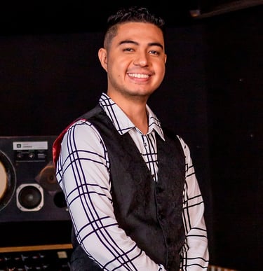 Bassist Ian Yoshio smiling, wearing a white shirt with black stripes and a black vest.