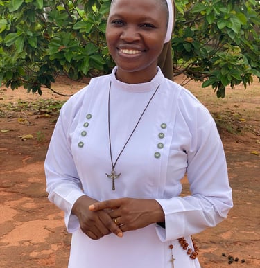 A smiling African Catholic nun wearing a white habit, crucifix necklace, and rosary beads outdoors.