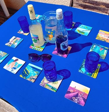 Dessous de verres paysages de Provence Realisart sur une nappe bleue.