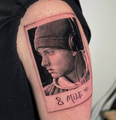 Tatuaggio ritratto in nero e grigio dettagliato di Eminem in una polaroid eseguito da Horidoku 