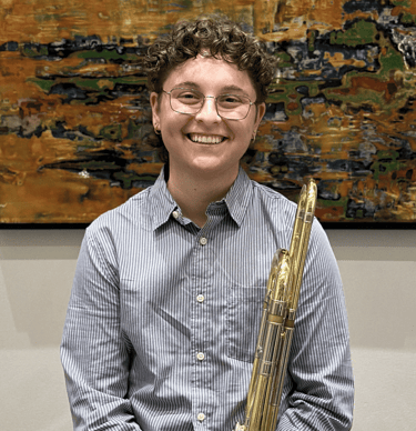 Natalie DiMundo in a blue shirt and glasses holding her trombone