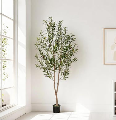 A tall artificial olive tree with realistic green leaves in a black pot stands in a bright, modern room.