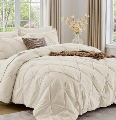 Sasttie 7-piece beige pinch pleat comforter set styled in a bright modern bedroom with neutral decor.