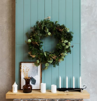 Elegant Christmas wreath made of eucalyptus and pine with bow hanging around a fireplace mantel.