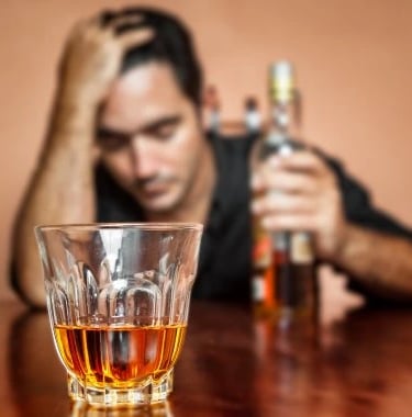 homme 1 bouteille d'alcool à la main gauche main droite sur la tête et verre devant lui presque vide