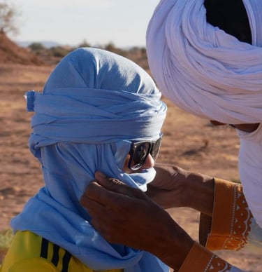 A nomad guide helps a boy arrange his cheche or head covering 