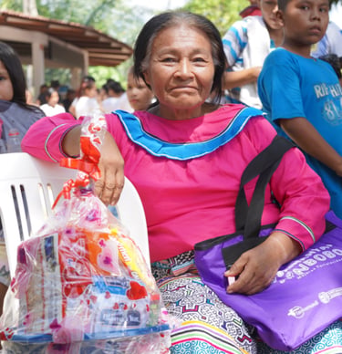 An indigenous woman in a pink blouse holding a gift basket at an event organized by Roger Bardales.