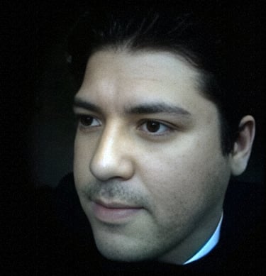 A close-up portrait of a dark-haired man looking away against a dark background.