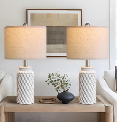 Pair of white textured ceramic table lamps with linen shades on a modern wooden console table.