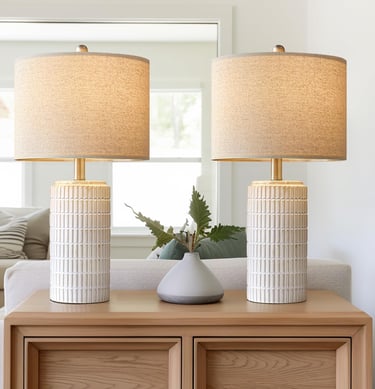 Pair of modern ceramic table lamps with textured white bases and linen shades on a wooden side table.
