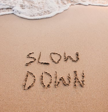 The words slow down written in the sand on a tropical beach with ocean waves.