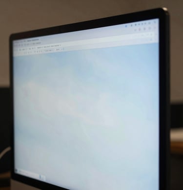 A close-up photograph of a designer in a North American / US creative studio, focused on a high-resolution screen reflecting soft sky blue tones.