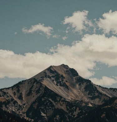 Minimalist wide shot of a solitary peak in the North American / US Cascades, surrounded by soft clouds, teal gray and off-white tones, calm and professional.