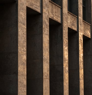 A close-up of a finished institutional concrete facade with sharp shadows cast by dramatic afternoon sunlight, warm bronze tones, 35mm