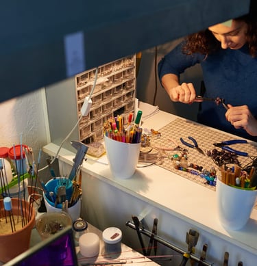 mujer sosteniendo herramientas de joyeria artesanal en mesa de trabajo con colores y material