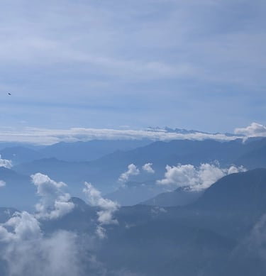 Panoramic mountain range view with blue misty peaks and white fluffy clouds under a bright sky. 
