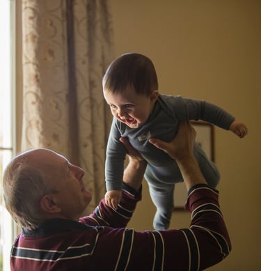Abuelo levantando a su nieto con una sonrisa, simbolizando la importancia de la estimulación cogniti
