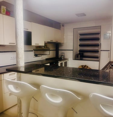 Cuisine moderne avec comptoir en granit noir, armoires claires et tabourets blancs.