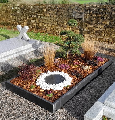 Sépulture moderne avec cadre en schiste, cercle de pierres blanches et paillis naturel.