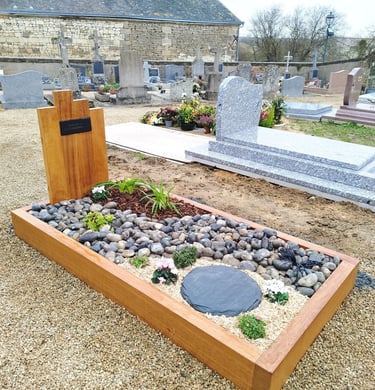 Aménagement funéraire avec encadrement bois, galets gris, schiste et fleurs de saison.