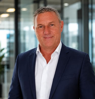 Professional portrait of a middle-aged male executive in a navy blue blazer and white shirt in a modern office.