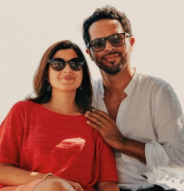 Due persone sedute all’aperto che sorridono, indossando occhiali da sole.