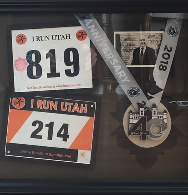 Shadow box display with I Run Utah marathon bibs, a 2018 finisher medal, and a commemorative photo.
