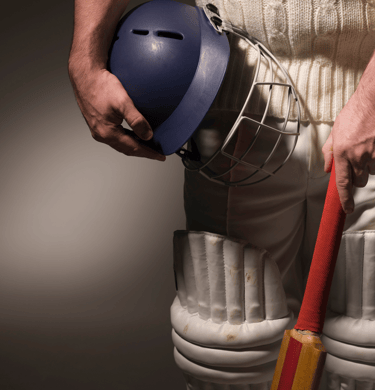 a man wearing white cricket uniform holding cricket bat and helmet and wearing pads