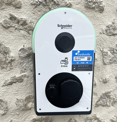 Borne électrique de recharge Schneider vu de face sur un mur en pierre
