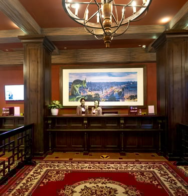 Luxury hotel lobby reception desk with friendly staff, wood paneling, and a large chandelier.
