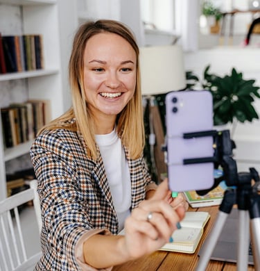 Smiling woman recording a video blog using a smartphone on a tripod for social media content.