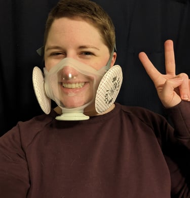 Melody throws a peace sign. She's wearing a transparent mask.