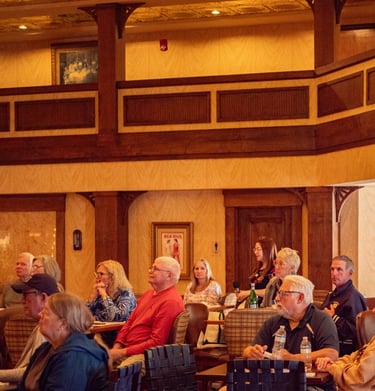 Audience seated in a warmly lit conference room, attentively listening to a presentation or speaker.