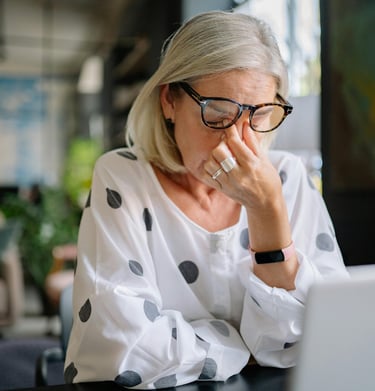 Anxious woman sits at her computer rubbing her eyes with tension