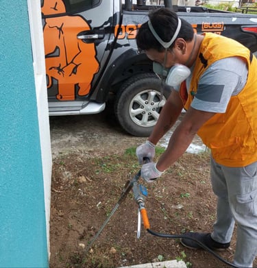 Professional pest control technician performing soil treatment for termite prevention near a home.