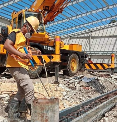 exterminator in safety gear near a yellow mobile crane at a steel frame building site.