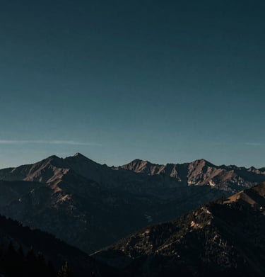A cinematic, wide landscape shot of mountains under a moody, deep midnight teal sky at dawn.