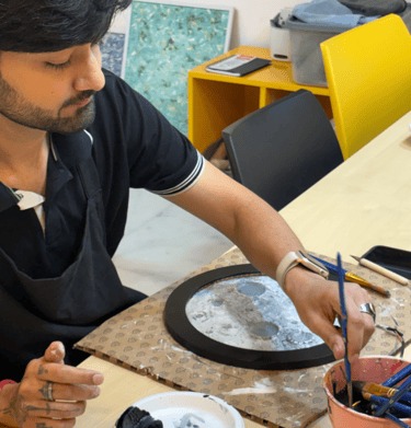 A male artist painting a circular moon lamp artwork using a brush and acrylic paints.