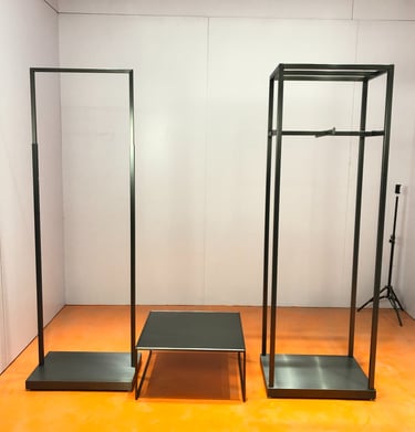 Modern minimalist black metal clothing racks and display table set for a retail fashion boutique.