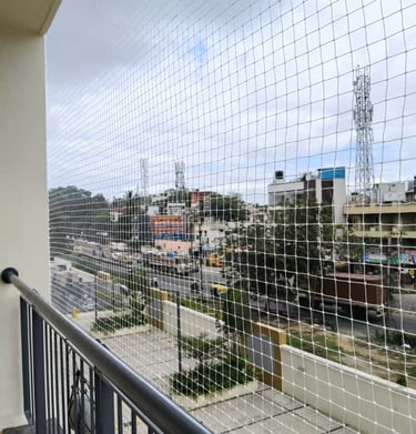 Wide shot of a balcony with a transparent safety net overlooking a bustling JP Nagar neighborhood.