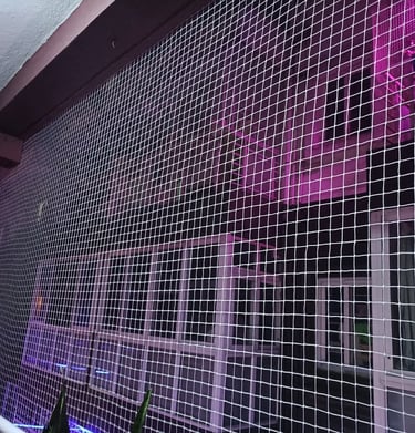 Evening shot of a balcony with pigeon netting, softly lit by warm indoor lights.