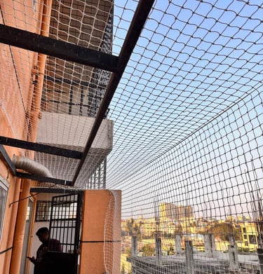 Wide shot of a spacious balcony fully covered with a fine mesh pigeon net, sunlight filtering throug
