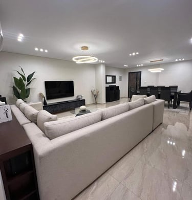 Modern open-plan living room with a large sectional sofa, flat-screen TV, and dining area.
