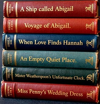 A stack of vintage hardcover books with gold embossed titles on colorful red, blue, and green spines.