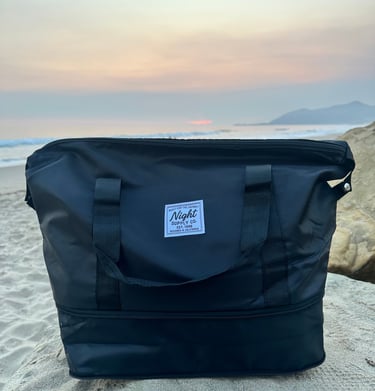 Black Night Supply Co. duffel bag on beach sand with sunset sky in background
