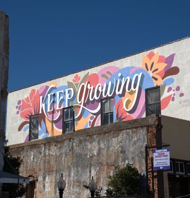 A colorful floral mural with the words Keep Growing painted on the side of a downtown brick building.