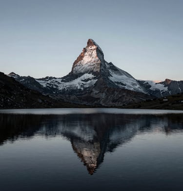 A minimalist composition of a lone peak reflecting in a perfectly still alpine lake during the blue hour. Tones of silver grey and jet black dominate. A cold, serene Global / Western mountain environment.