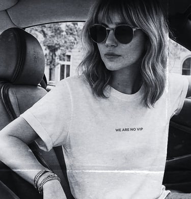 Black-and-white photo of a woman in sunglasses wearing the NOVIP ‘We Are No VIP’ T-shirt inside a ca