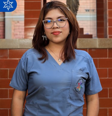 a woman in scrubs and glasses standing in front of a brick wall