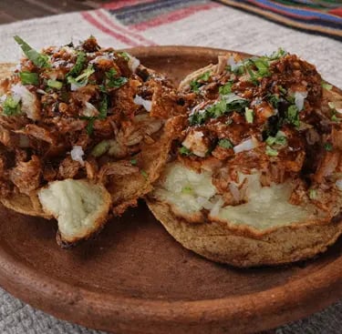 Volcanes de barbacoa de res con queso fundido, salsa roja y cilantro en Querétaro.